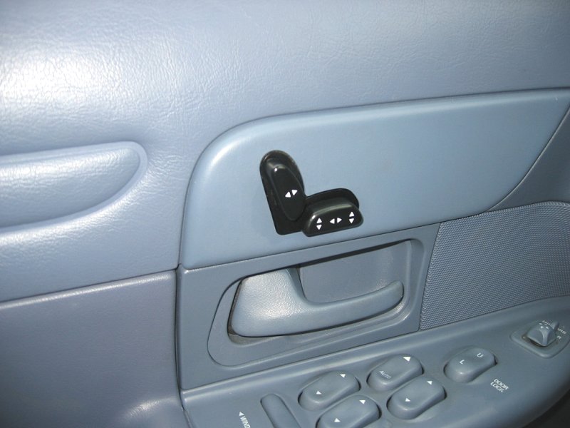Power seat controls on a light blue interior door panel with a door handle and window controls