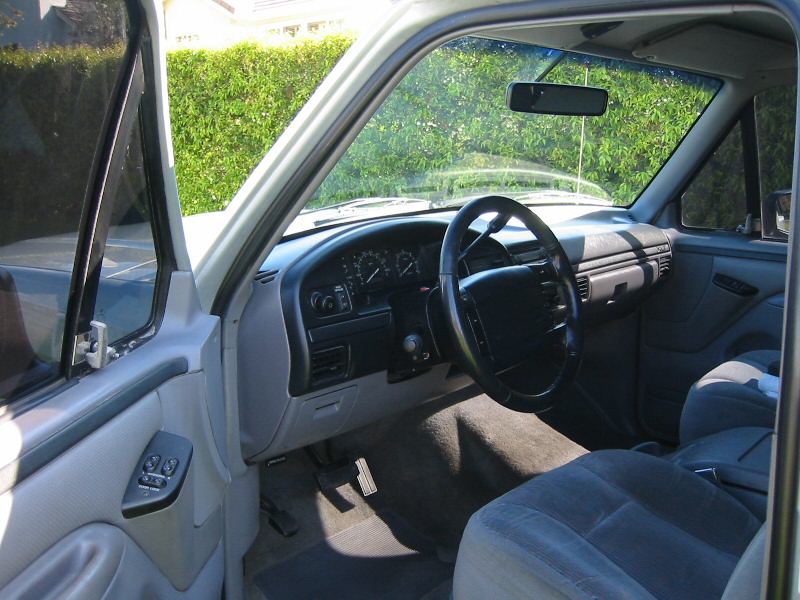Gray interior of a Ford truck/SUV seen through open driver's door, cloth seats and steering wheel visible