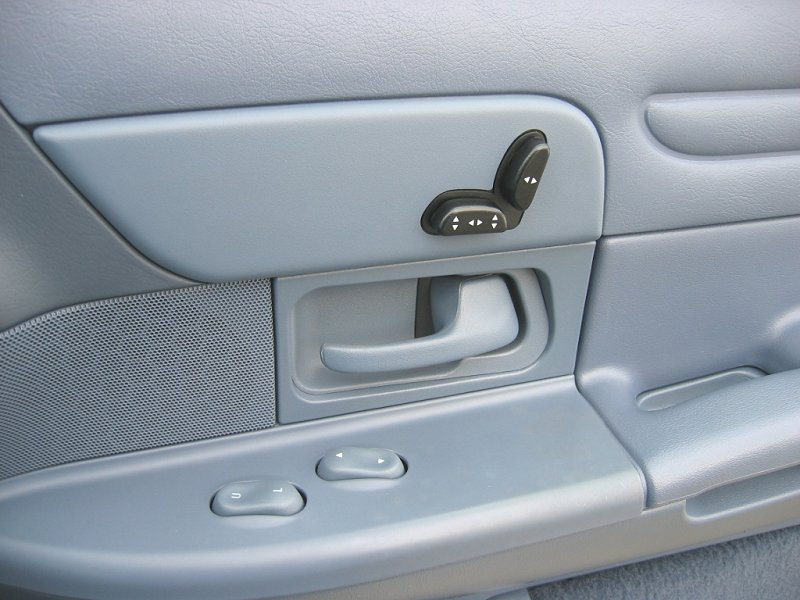 Close-up of a car's interior door panel, showing power seat controls, door handle, and window controls