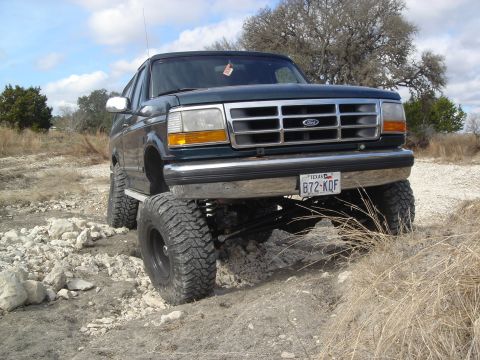 1995 Ford Bronco - This lifted Ford Bronco is navigating a rough, rocky terrain under a cloudy sky.