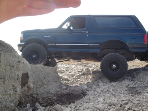 1995 Ford Bronco - A dark green Ford Bronco is shown from the side, navigating a rocky, off-road path.