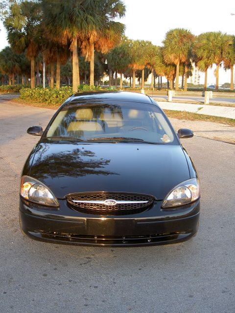 2003 Ford Taurus - Frontal view of a black 2003 Ford Taurus, parked on asphalt with palm trees lining the street.
