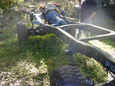 1989 Ford Bronco - The chassis of a vehicle, including the engine and transmission, sits on grassy ground.
