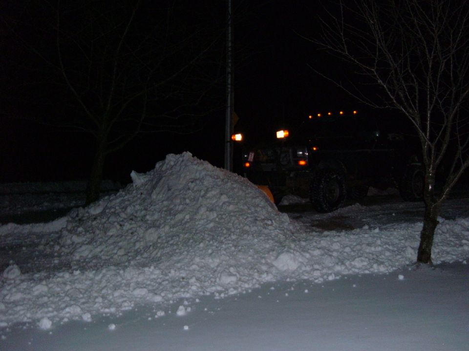 Truck with snow plow parked next to a large pile of snow at night