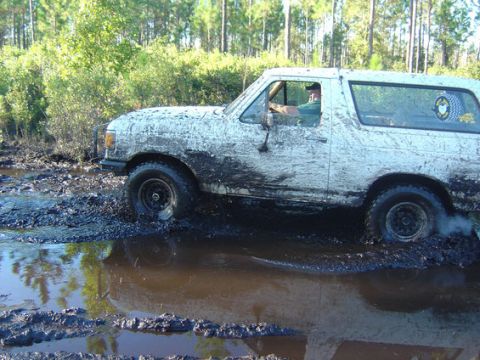 1989 Ford Bronco - This muddy SUV is navigating a challenging off-road obstacle, with its tires deep in the muck.