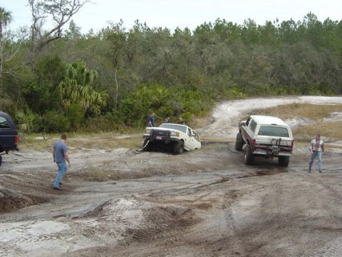1989 Ford Bronco - Two Ford Broncos navigate a muddy off-road course with onlookers.