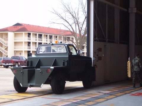 1988 Ford Bronco - A green flatbed truck with a unique custom bed is parked near a building entrance, with another truck visible in the background.