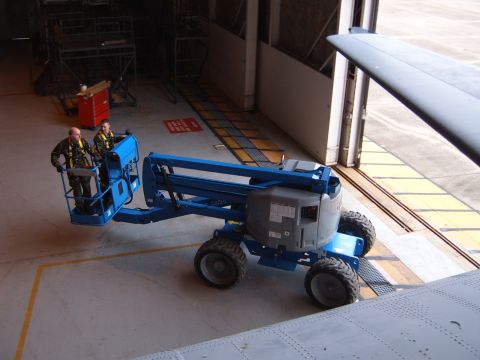 1988 Ford Bronco - Two individuals operate a boom lift inside a hangar, positioned near a large aircraft.