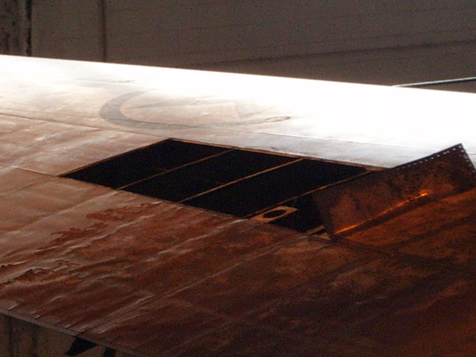 Rusty metal panel with a rectangular cutout and internal grid, showing a curved line marking