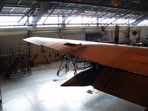 1988 Ford Bronco - An airplane wing is visible inside a large hangar, surrounded by maintenance equipment and scaffolding.