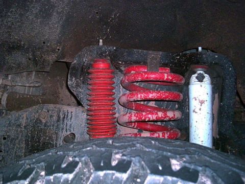 1988 Ford Bronco - Vehicle suspension components including a red coil spring and shock absorber with bellows.