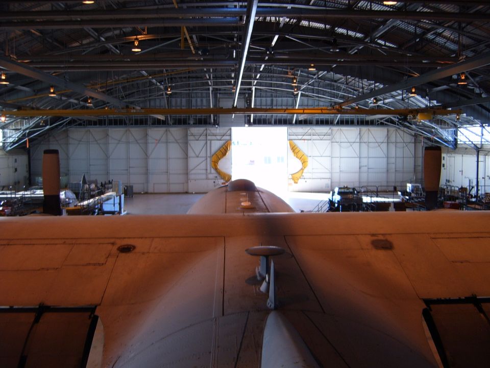 Aircraft hangar interior with a large aircraft wing in the foreground and a Supermotors.net watermark
