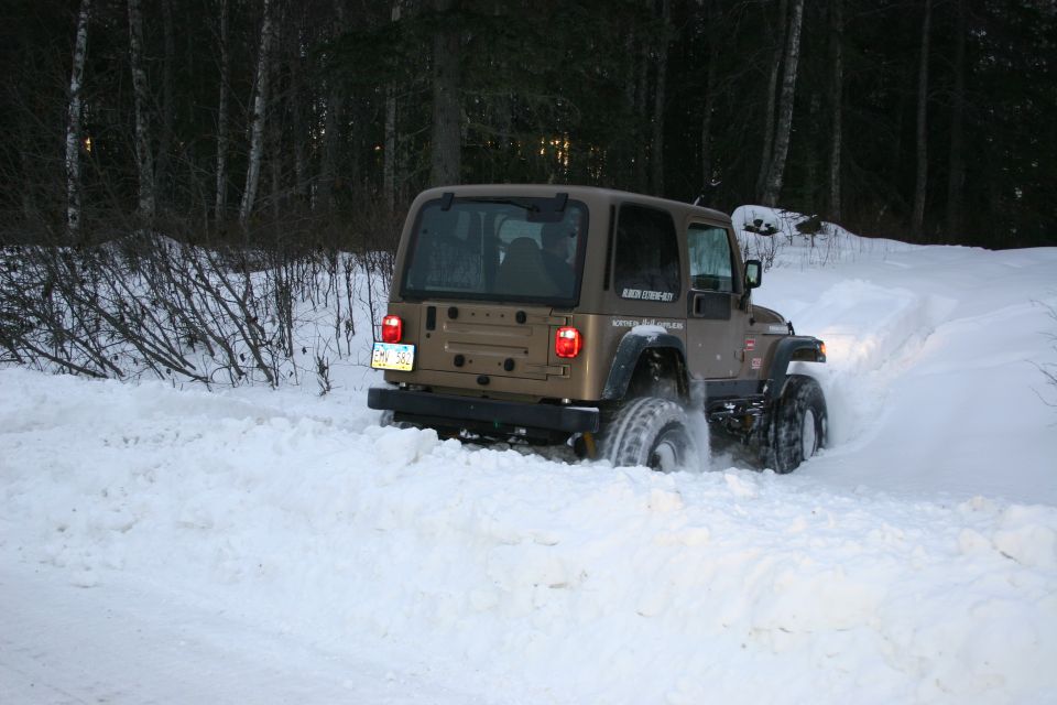 Brown Jeep TJ driving through deep snow, trees in background
