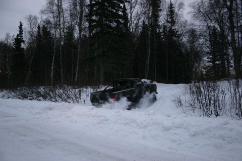 2003 Jeep TJ - Pickup truck with camouflage paint and roll bar driving through deep snow.