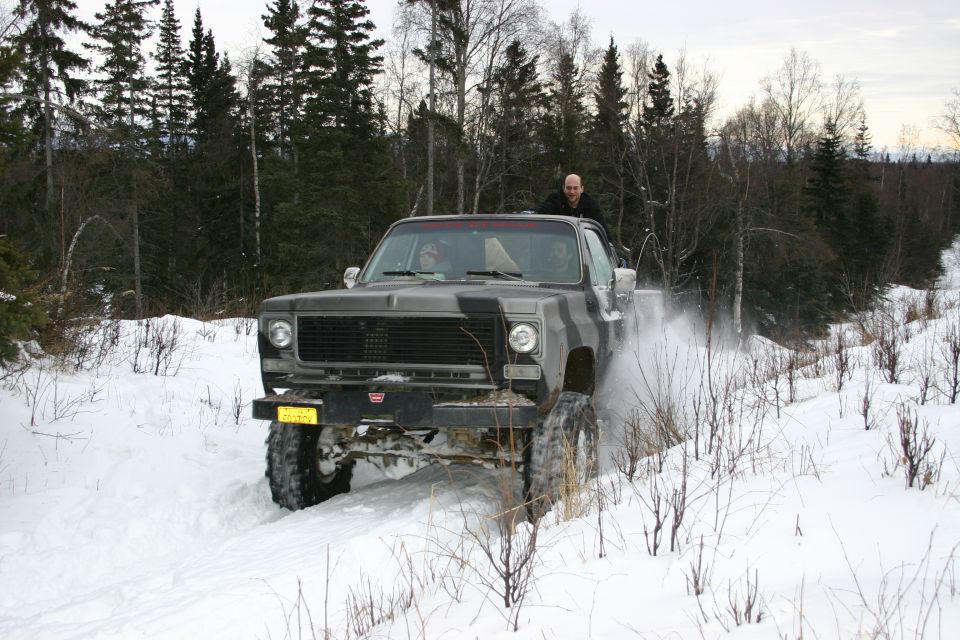 Gray camouflage pickup truck driving through snow, kicking up spray