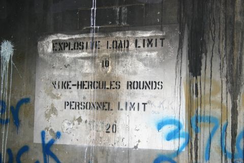 2003 Jeep TJ - A weathered sign with warnings about explosive load and personnel limits is defaced with graffiti and water damage.
