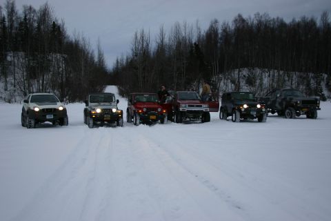 2003 Jeep TJ - A group of off-road vehicles, including multiple Jeep TJs, are parked in a snow-covered area with trees in the background.