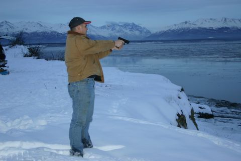 2003 Jeep TJ - Man aims handgun in snowy landscape with mountains and frozen water.