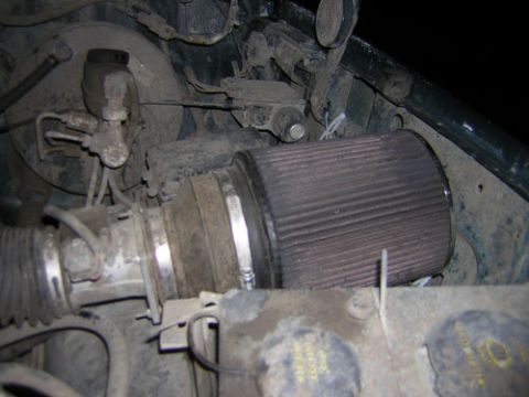 1995 Ford Bronco - Dusty engine bay close-up of a conical cone-style air filter clamped to a metal intake tube feeding a mass air sensor, with a flexible corr…