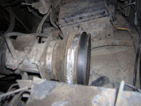 1995 Ford Bronco - Dusty engine bay close-up showing a rubber intake duct secured with a worm-gear hose clamp where it meets the air intake or throttle body h…