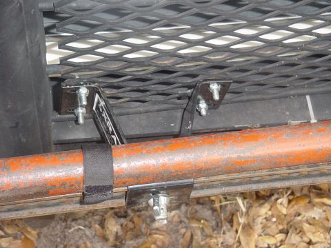 1989 Ford Bronco - A Hi-Lift Jack is secured to a vehicle's rack system with metal brackets and a strap.