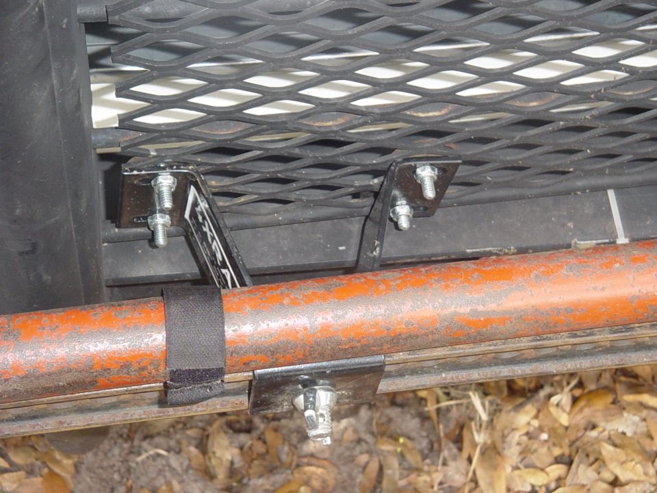 Hi-Lift Jack mounted with brackets to a vehicle rack, showing orange pipe and black strap
