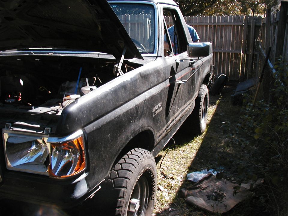 Black 1989 Ford Bronco with hood open, parked outside next to a wooden fence