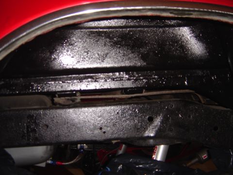 1978 Ford Bronco - Close-up view of the underbody chassis and wheel well of a red vehicle, showing protective black coating.