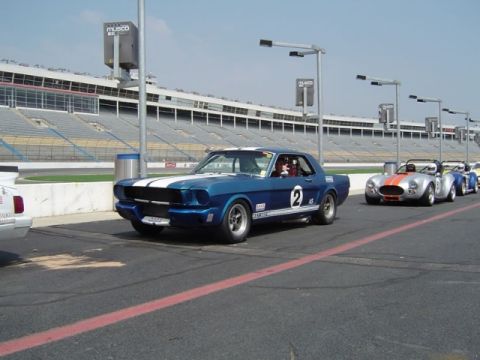 1965 Ford Mustang - A blue 1965 Ford Mustang race car with white stripes and the number 2 is on the track, with other cars in the background.
