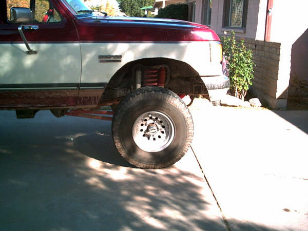 Front wheel of lifted maroon and silver Bronco showing red coil shock