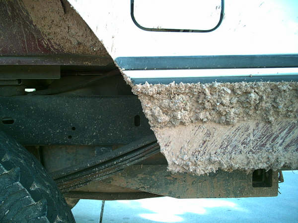 Underside rocker of a truck caked with dried mud above a leaf spring