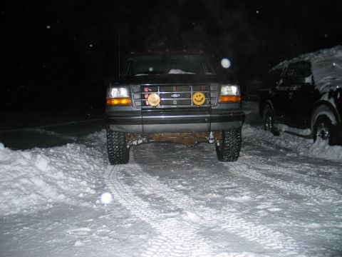 1995 Ford Bronco - Head-on night flash photo of a lifted dark-colored Ford truck parked in deep snow, with cab clearance lights on the roof and snow piled on…
