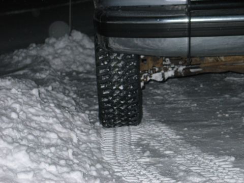 1995 Ford Bronco - Night shot of the driver-side rear wheel of a silver truck or SUV parked in deep snow, showing an aggressive all-terrain tire biting into p…