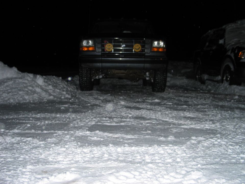 Lifted dark Ford 4x4 at night in snow with yellow smiley-face light covers in grille