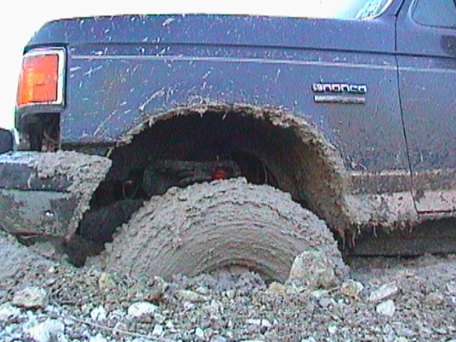 1989 Ford Bronco stuck deep in mud, front fender and wheel visible