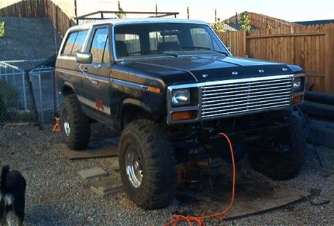 1986 Ford Bronco - This lifted 1986 Ford Bronco features a black body with a white roof and prominent off-road tires.