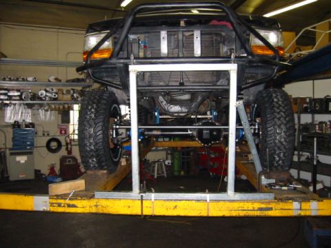 1992 Ford Bronco - This heavily modified truck is elevated on a lift in a workshop, showing its undercarriage and suspension modifications.