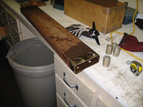 1992 Ford Bronco - A rusty metal beam with mounting holes sits on a workbench next to tools and parts.
