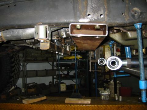 1992 Ford Bronco - Underbody shot of a truck on a lift showing a newly fabricated bare-steel crossmember/mount bolted to the frame rail, with a heim-joint lin…