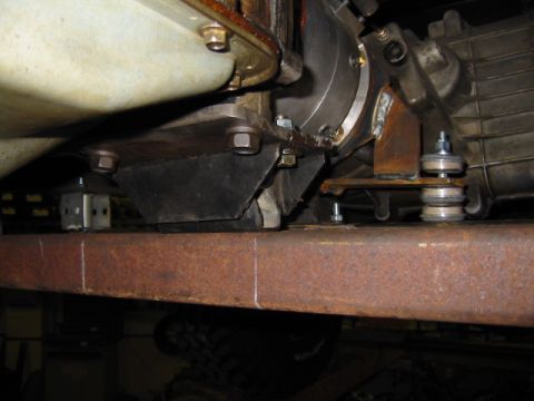 1992 Ford Bronco - Underside close-up of a transmission snubber bolted through a new bare-steel crossmember, with the transmission tailhousing, bellhousing an…