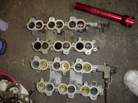 1998 Ford Taurus - Three intake manifolds are shown on a concrete surface, alongside a red flashlight and cleaning supplies.