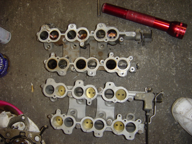 Three aluminum intake manifolds with four ports each, laid out on a concrete surface