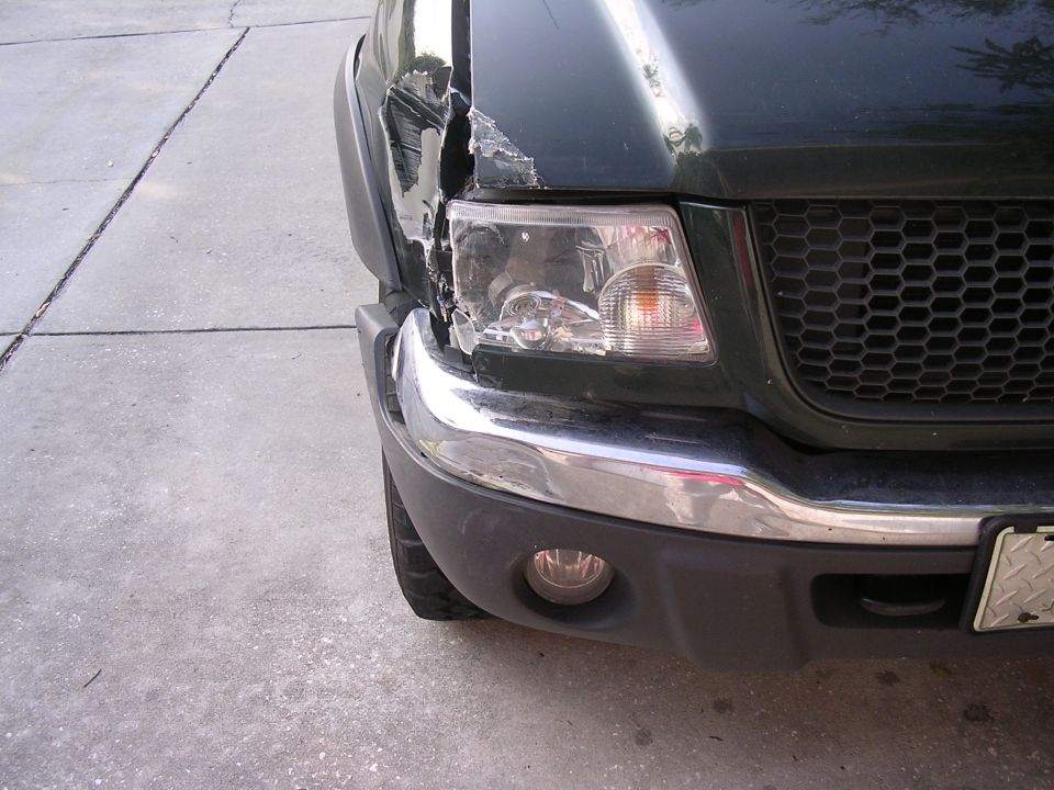 Damaged dark green pickup truck front end with dented fender and broken headlight
