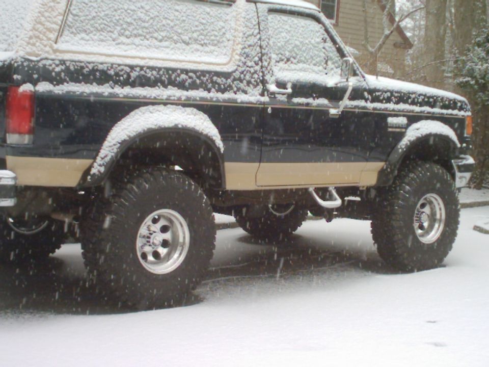Side view of a lifted Ford Bronco with large tires, covered in snow
