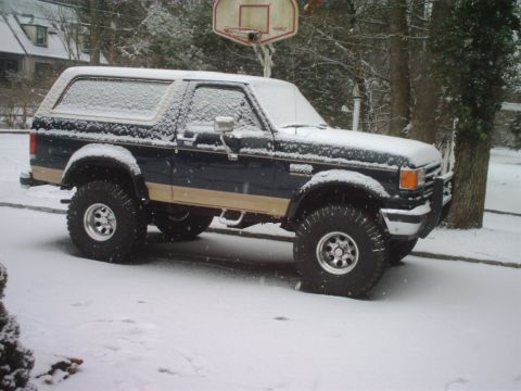 1989 Ford Bronco - This lifted Bronco, likely from the late 1980s, sits covered in snow with off-road tires.