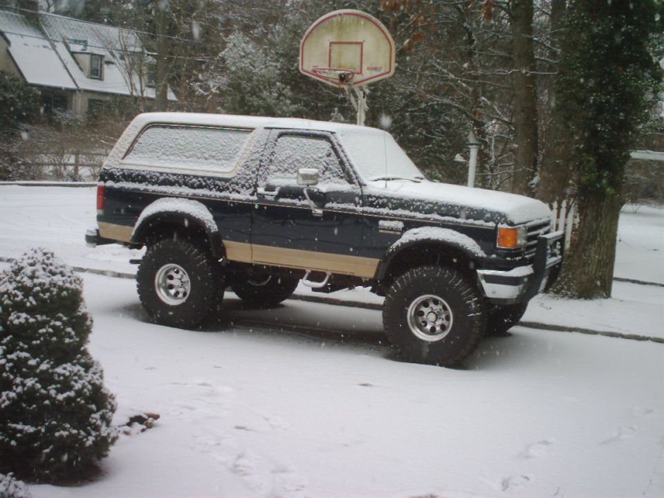 Dark blue and tan Ford Bronco with lifted suspension parked in snow