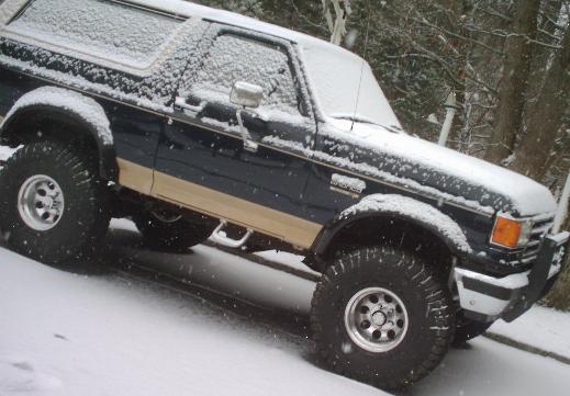 Lifted blue and tan Ford Bronco with white top covered in falling snow
