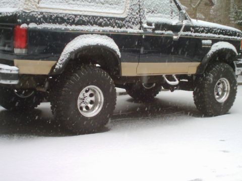 1989 Ford Bronco - A lifted Ford Bronco with off-road tires is seen covered in snow.