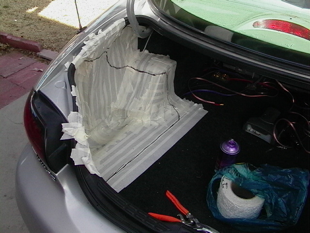 Car trunk with a mold for a subwoofer enclosure being made with tape and paper. Tools and supplies are in the trunk