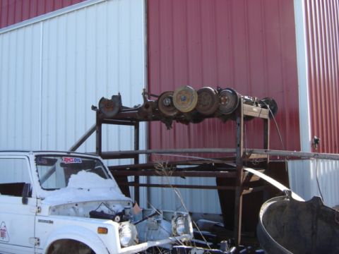 1992 Ford Bronco - A white SUV sits in front of a building with a rack of vehicle axles behind it.